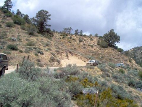 1988 Ford Bronco - Two trucks navigate a steep, arid hillside road under a cloudy sky.