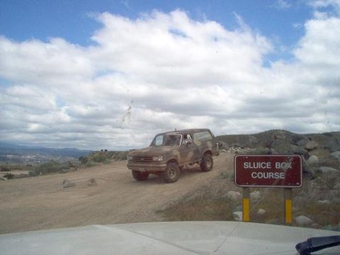 1988 Ford Bronco - A 1988 Ford Bronco drives on a dirt road with a sign for the Sluice Box Course in the foreground.