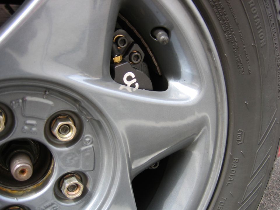 Close-up of a car's wheel, showing lug nuts and a black brake caliper with a white 'CS' logo