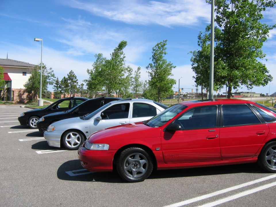Red Ford Taurus SHO sedan parked in a row with silver and dark Tauruses behind it