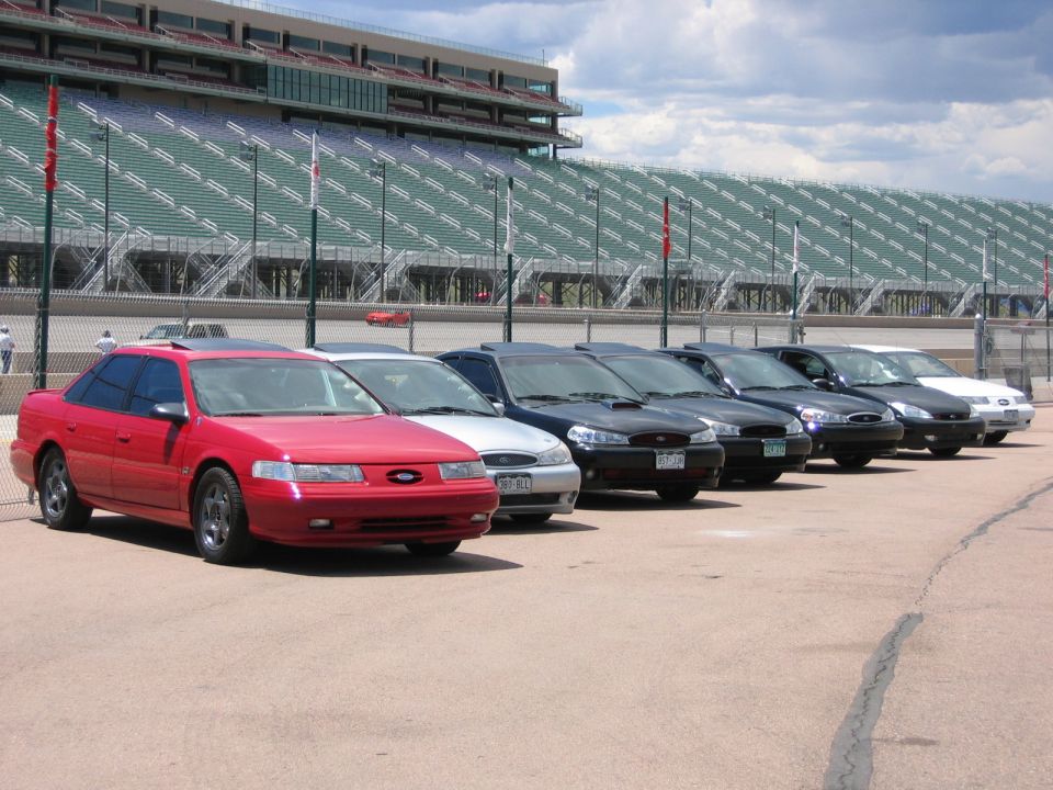 Row of Ford Taurus sedans parked at a speedway in front of empty grandstands