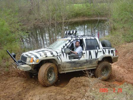 1993 Jeep Grand Cherokee - A modified Jeep Grand Cherokee with a zebra pattern navigates a challenging muddy off-road course.
