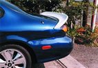 1999 Ford Taurus - Close-up of the rear quarter panel of a blue car, a white aftermarket spoiler and distinctive wheels.