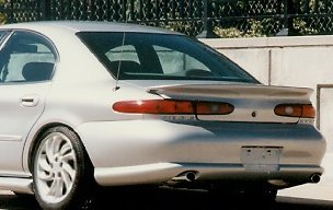 1999 Ford Taurus - Small three-quarter rear view of a silver Mercury Sable sedan parked beside a chain-link fence, showing its full-width light bar taillight…