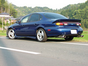 1999 Ford Taurus - Small rear three-quarter shot of a dark blue four-door sedan on a rural road, showing a large trunk-lid spoiler, chrome dual exhaust tips a…