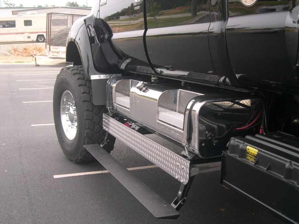 Black heavy duty truck with large tires, chrome fuel tanks, and diamond plate steps