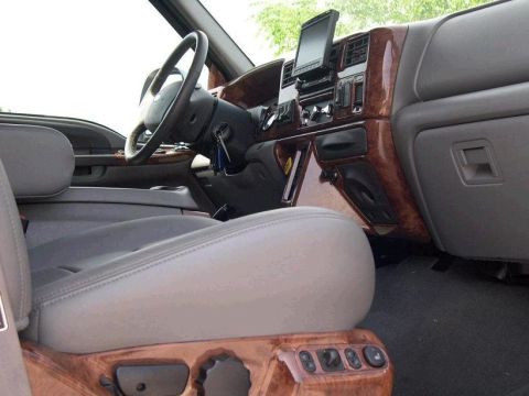 1989 Ford Bronco - The interior of a truck features wood grain trim, gray leather seats, and a mounted screen on the dashboard.
