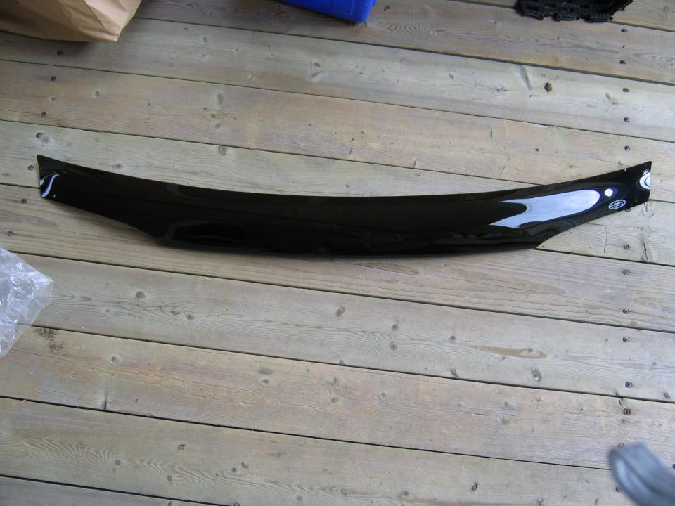 Black bug deflector with a subtle curve, resting on a wooden floor