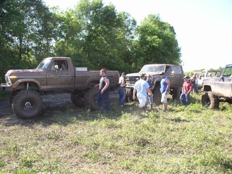 2000 Chevrolet Tahoe - Several lifted pickup trucks are gathered in a muddy field with people around them.