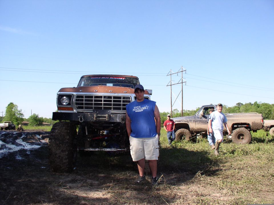 Lifted brown Ford truck front view in muddy field with people