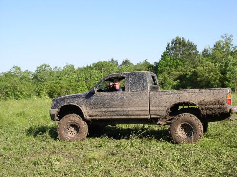 2000 Chevrolet Tahoe - A driver navigates a muddy pickup truck through a field with trees in the background.