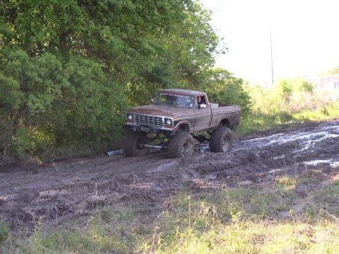 2000 Chevrolet Tahoe - This lifted pickup truck is navigating a challenging muddy terrain, kicking up mud as it goes.