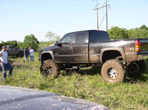 2000 Chevrolet Tahoe - A heavily modified pickup truck, caked in mud, sits in a grassy field with other vehicles and people nearby.