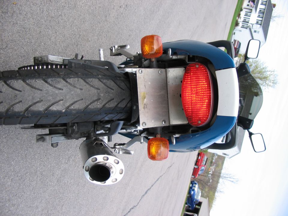 Rear view of a blue and white motorcycle showing taillight, turn signals and chrome exhaust