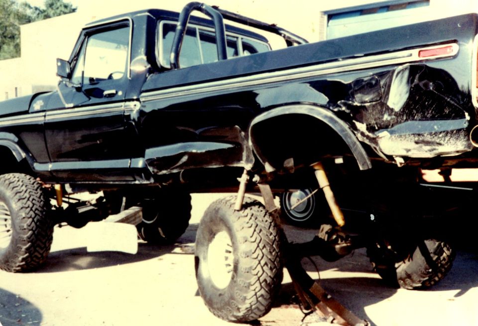 Black lifted Ford F-150 pickup with crushed rear bed, on large off-road tires