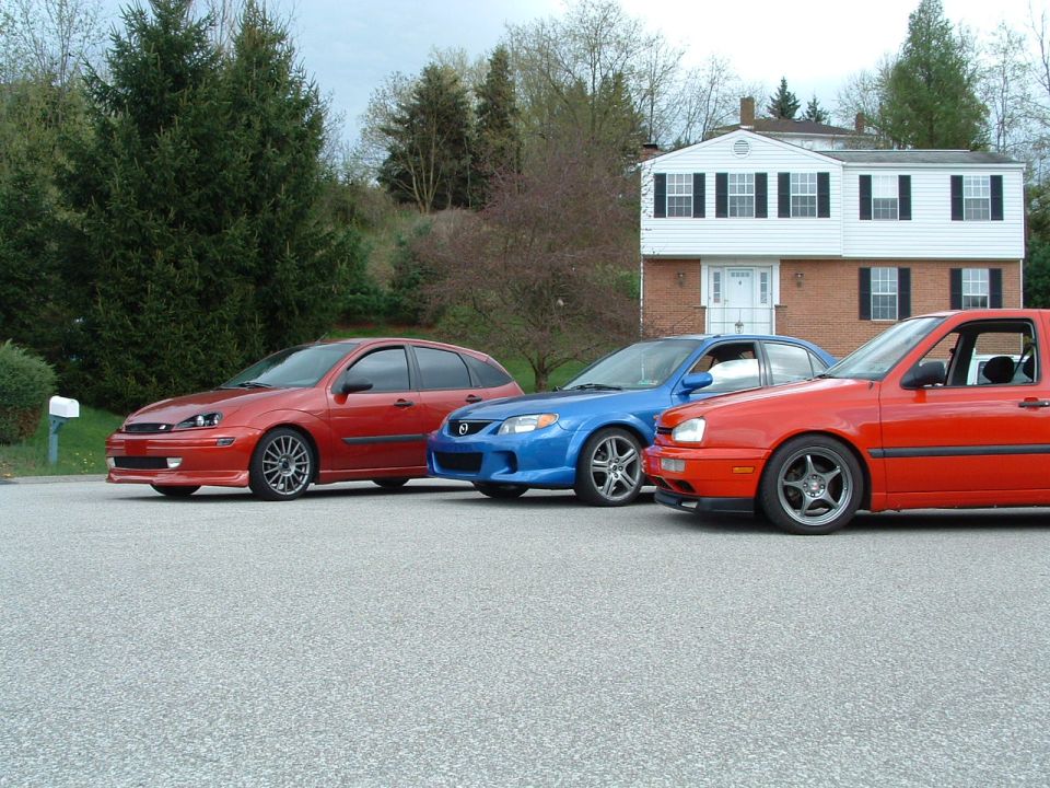 Red 1999 Ford Focus hatchback parked in front of a house with two other cars