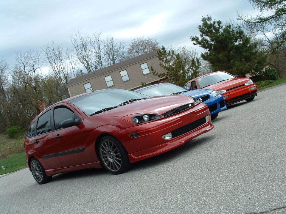 Red hatchback, blue sedan, and red coupe parked on a street
