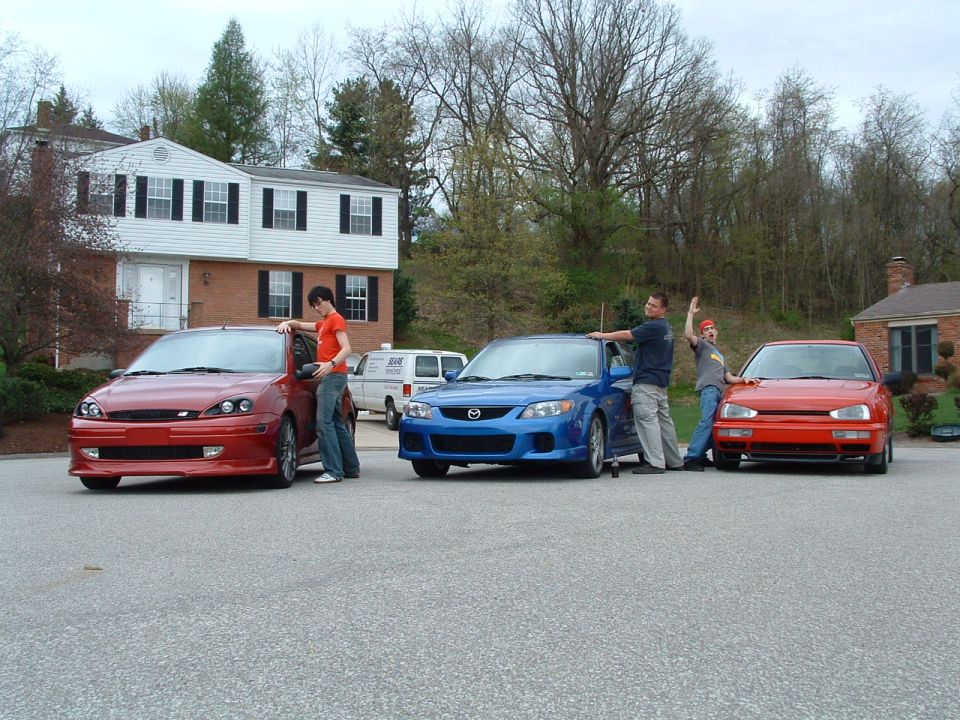 Red Ford Focus, blue Mazda, and red car with people standing by them