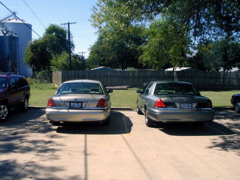 2000 Ford Crown Victoria - Two Ford Crown Victorias are seen from the rear in a parking lot setting.