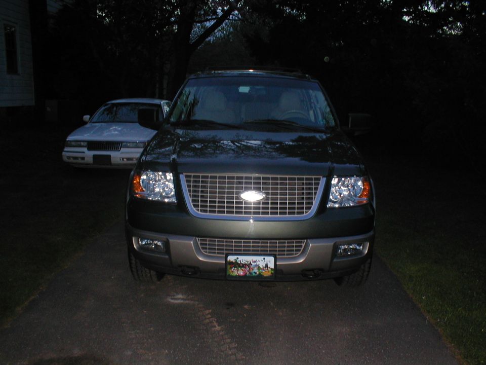 Front view of dark green SUV with chrome grille and headlights. License plate visible