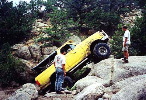 1988 Ford Bronco - A yellow off-road truck is navigating a difficult rocky terrain with two men observing the action.