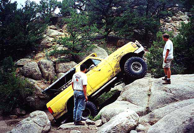 Yellow Ford Bronco climbing steep boulders on a rocky off-road trail with two onlookers