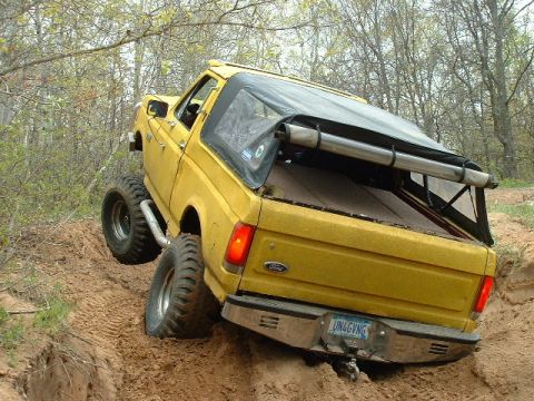 1988 Ford Bronco - A yellow pickup truck navigates a steep dirt incline with its tires digging into the soil.