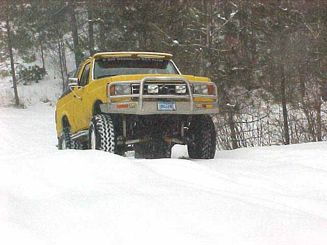 Yellow lifted pickup with brush bar and big tires in deep snow among trees