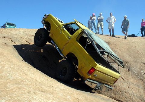 1988 Ford Bronco - A modified pickup truck navigates a challenging off-road trail with spectators observing the ascent.