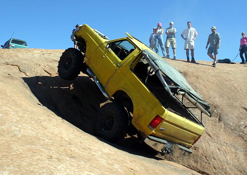 Yellow topless Ford Bronco climbing down steep slickrock as spectators watch