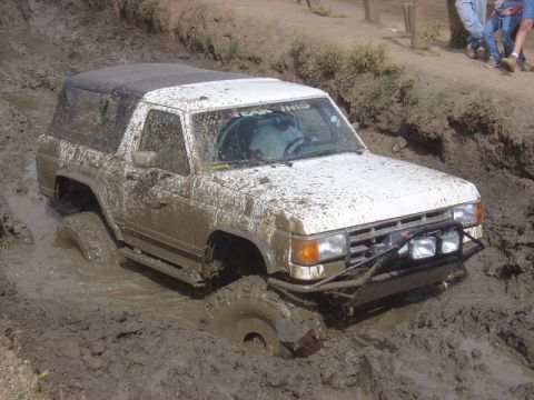 1978 Ford Bronco - White SUV struggling in deep mud, with "TEAM THIS" visible on the windshield.