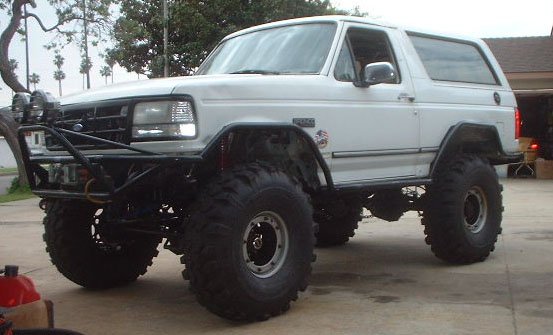 White 1992 Ford Bronco with large off-road tires, custom bumper, and auxiliary lights