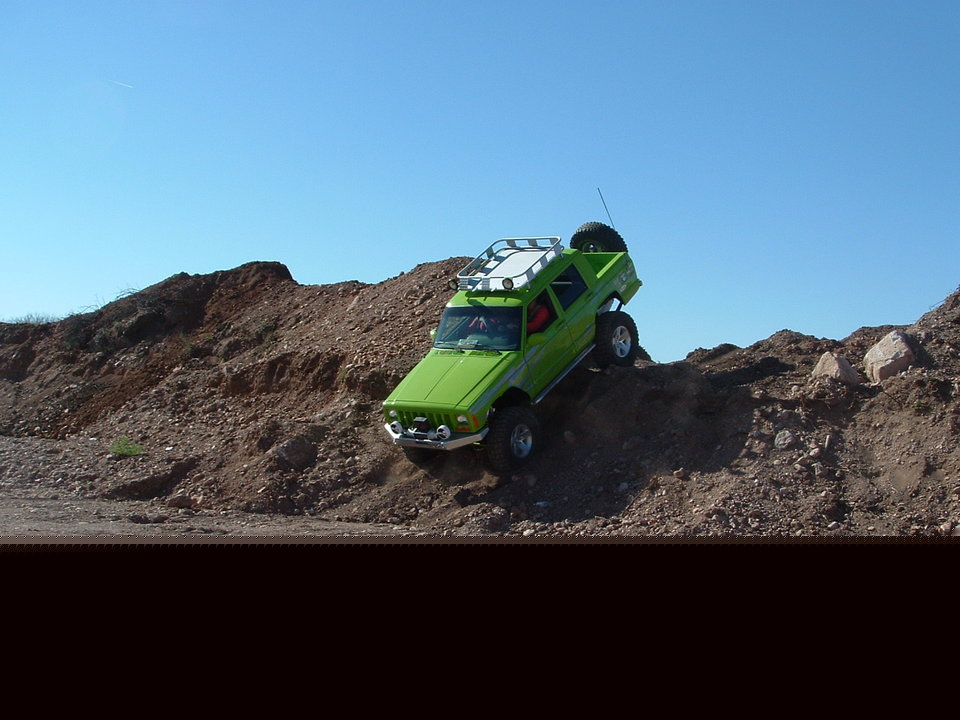 Green Jeep Cherokee climbing a dirt hill, with a roof rack and spare tire visible