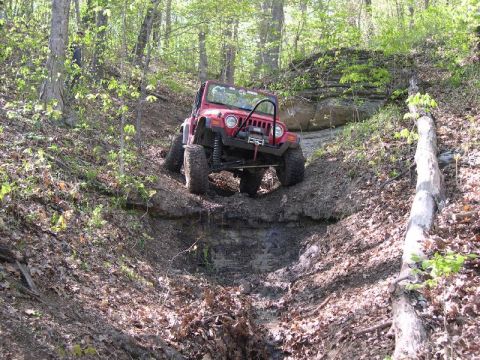 1999 Jeep TJ - This red 1999 Jeep TJ tackles a challenging offroad course, demonstrating its capability on steep, muddy terrain.