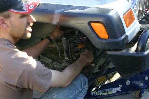 2003 Jeep TJ - A person is working on the front suspension of a Jeep TJ, which is supported by a blue hydraulic jack.