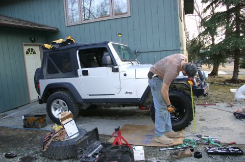 2003 Jeep TJ - Man measures a tire on a 2003 Jeep TJ parked in a driveway.