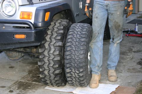 2003 Jeep TJ - A person stands next to a silver Jeep TJ, comparing two large off-road tires. The registry claims it is a 2003 model, but year evidence is…