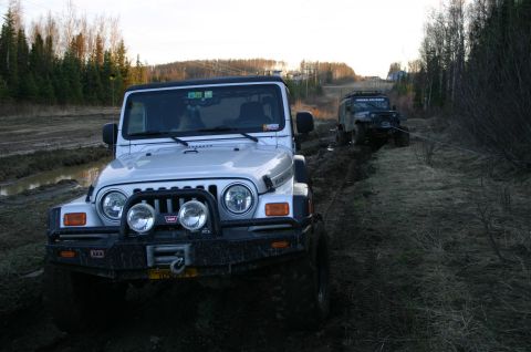 2003 Jeep TJ - Two Jeeps navigate a muddy trail, with one appearing to tow the other.