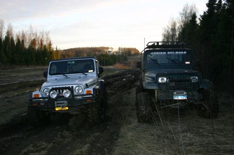 2003 Jeep TJ - Two 2003 Jeep TJs navigating a muddy off-road trail under a cloudy sky.