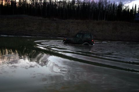 2003 Jeep TJ - A camouflaged Jeep navigates through a body of water, leaving distinct tire tracks in its wake.