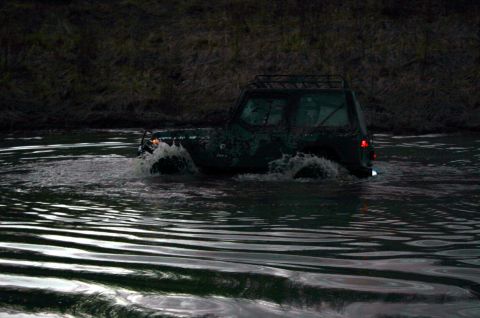 2003 Jeep TJ - A dark green Jeep Wrangler navigates through a body of water, creating splashes as it moves.