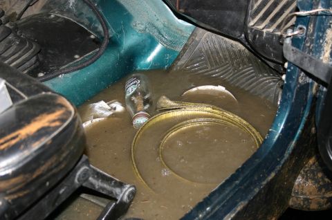 2003 Jeep TJ - The interior of a vehicle is flooded with murky water, containing a glass bottle and a yellow strap.