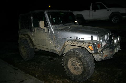 2003 Jeep TJ - A muddy silver 2003 Jeep TJ Rubicon is parked at night, with a white pickup truck in the background.