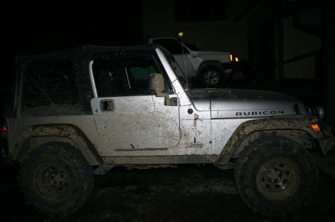 2003 Jeep TJ - Mud-covered 2003 Jeep TJ Rubicon parked next to a white SUV in the dark.