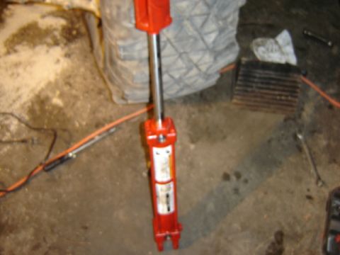 1989 Ford Bronco - A red hydraulic jack is shown on a concrete floor with some tools and a large tire in the background.