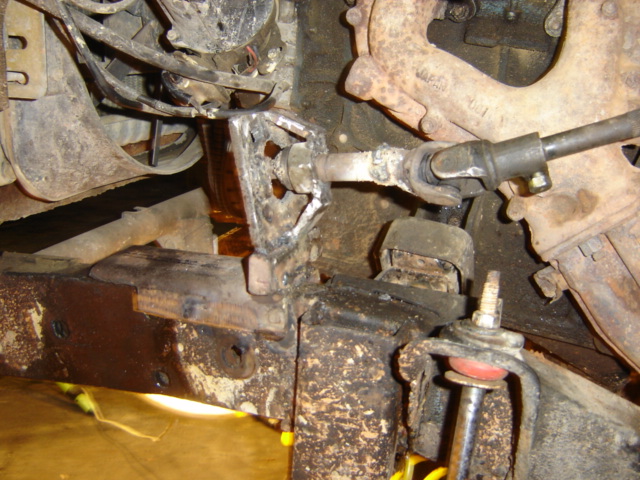 Rusty steering linkage and suspension parts on a vehicle underside. Visible text: SUPERMOTORS www.supermotors.net