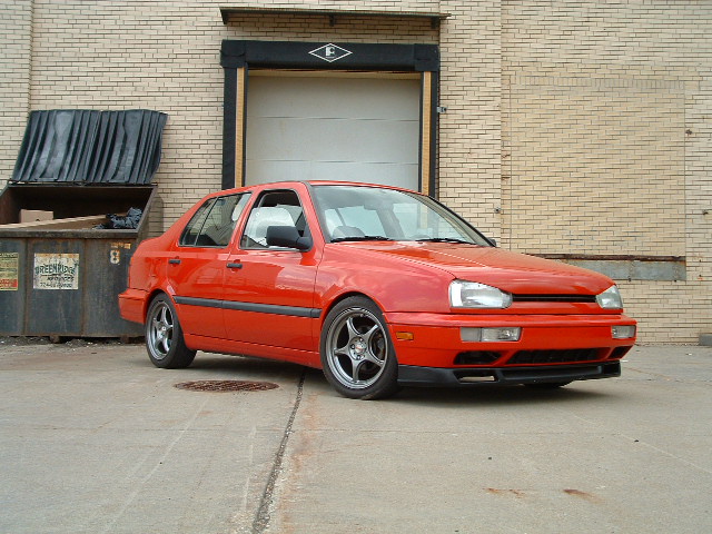 Red 1994 Volkswagen Jetta sedan parked outside a brick building with a garage door