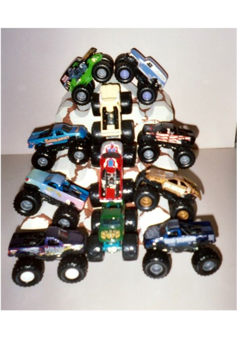 1979 Ford Bronco - A variety of toy monster trucks are arranged in a pile on a light-colored surface.
