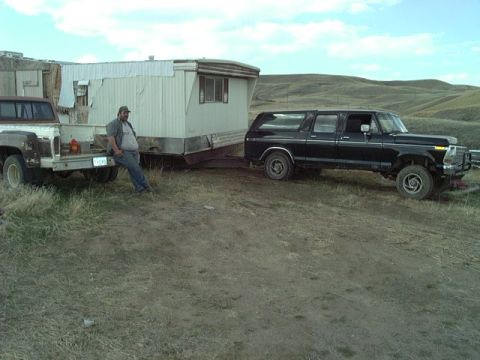 1979 Ford C-250 (Centurion Conversions) - A man leans on a pickup truck while a black SUV tows a trailer in a rural setting.