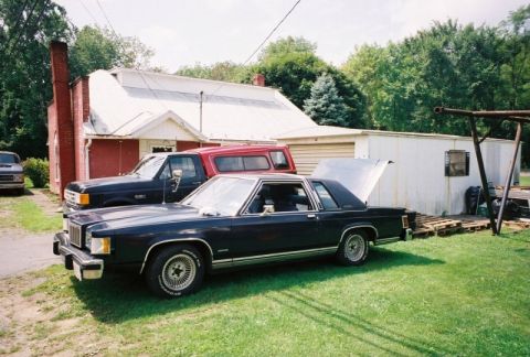 1984 Mercury Grand Marquis - A 1984 Mercury Grand Marquis coupe sits in a yard with its hood and trunk open, parked next to a pickup truck.
